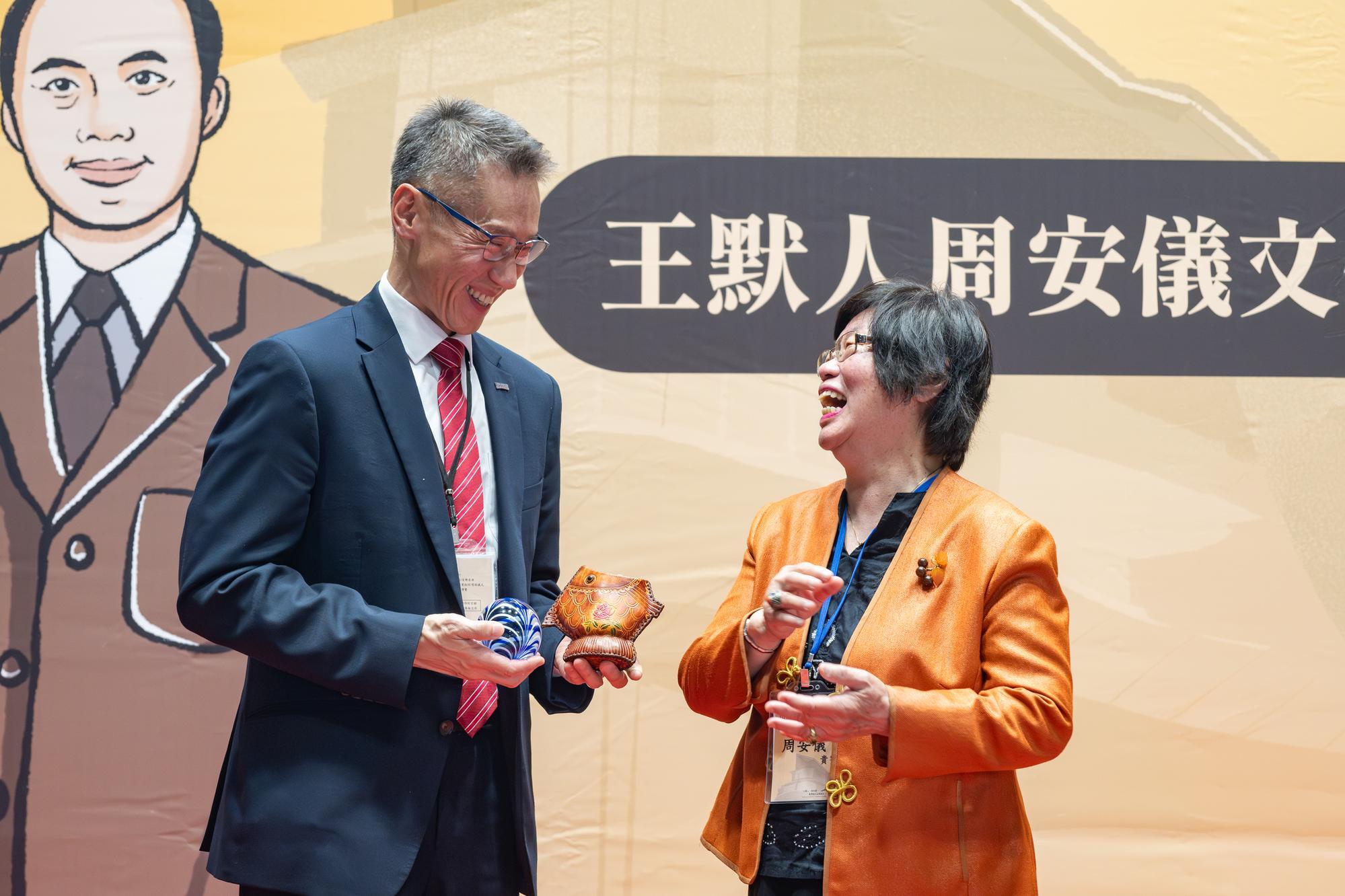 Ms. An-Yi Chou (周安儀) (right) presents a pen holder and a glass paperweight to President W. John Kao (高為元), expressing her wish that NTHU will prosper in its literary endeavors.