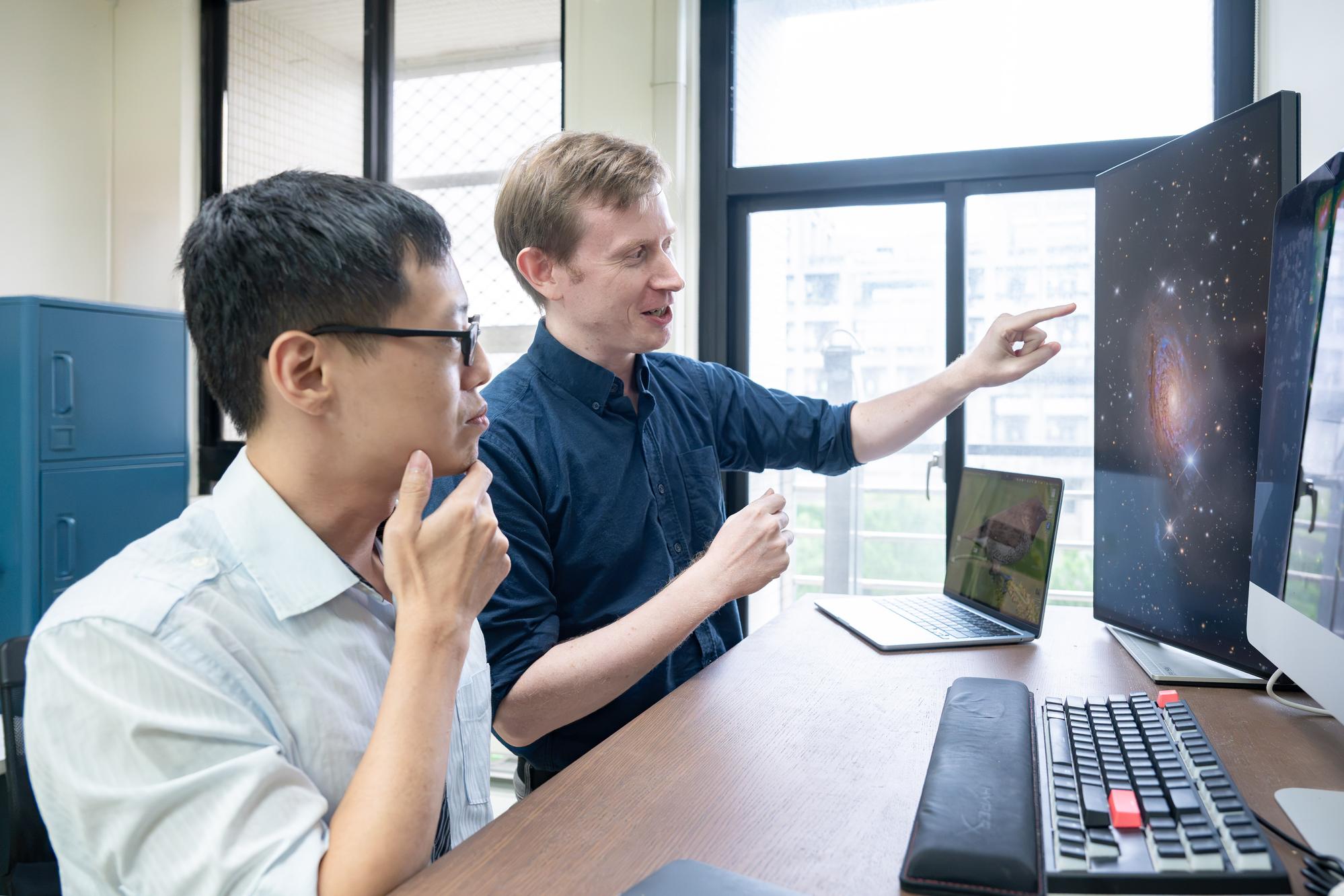 NTHU Associate Professor Andrew Cooper (right) explains that the faint structures surrounding galaxies preserve clues to their growth histories. At left is doctoral student Chung-Wen Wang.